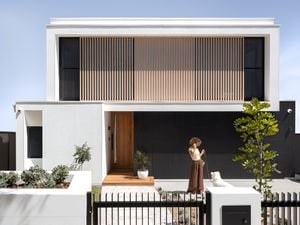Front yard view of white and black exterior house with woman holding dog on a leash.