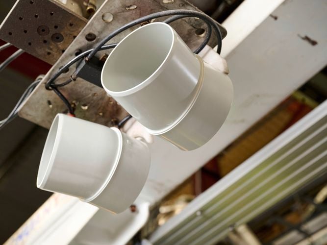 Two
  white PVC plumbing fittings suspended by machinery in a manufacturing
  facility