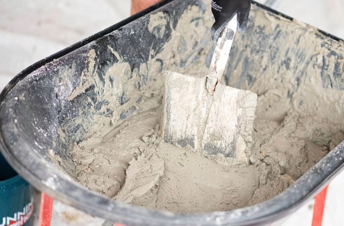 A person is adding water slowly to the dry mix and mixing it with a shovel until the mortar reaches the right consistency.