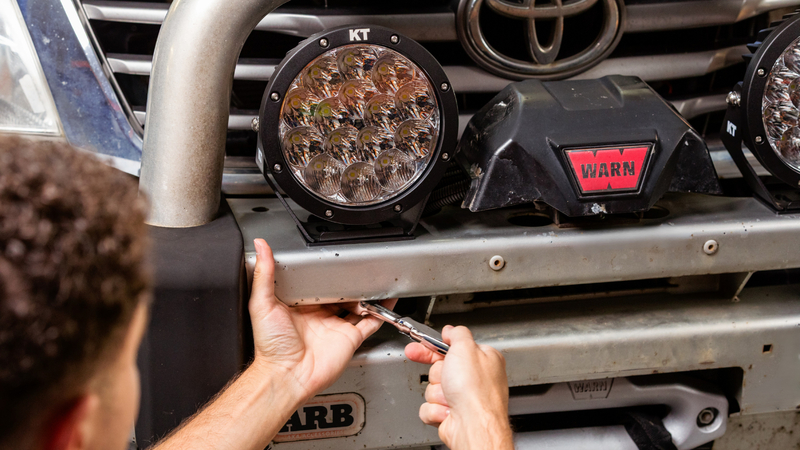 Person installing KT 7'' LED driving light onto front bull bar of Toyota Hilux.