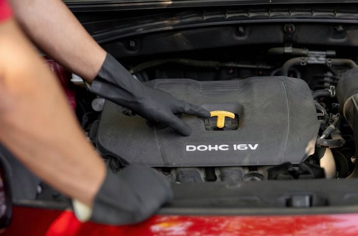 a person wearing black gloves pressing down the oil dipstick into a car engine after completing an oil check or refill. 