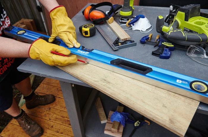 Person using spirit level to mark piece of timber with pencil.
