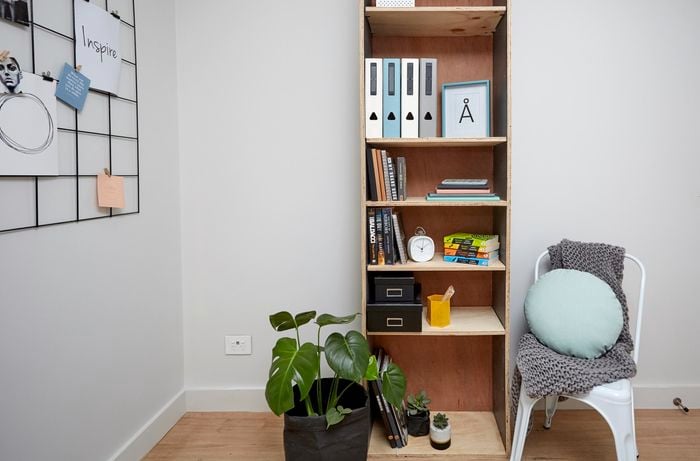 A narrow timber shelving unit next to a potted plant and chair