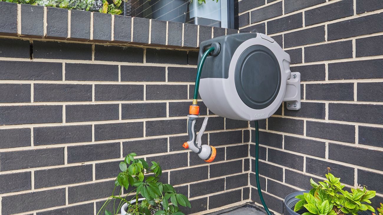 A hose reel sits mounted on a black, brick wall