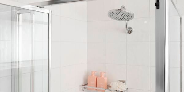 A new shower head and neatly organised shampoo and conditioner on a wall shelf.