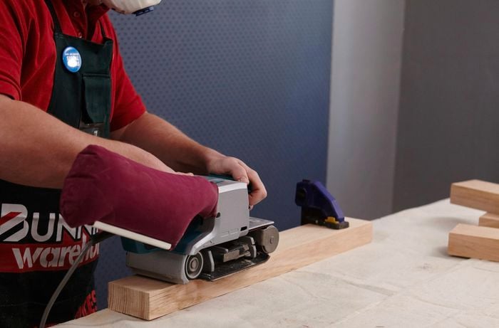 A belt sander being used to sand down a length of timber