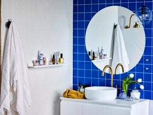 Bathroom with round mirror, brass tap and blue tiles.