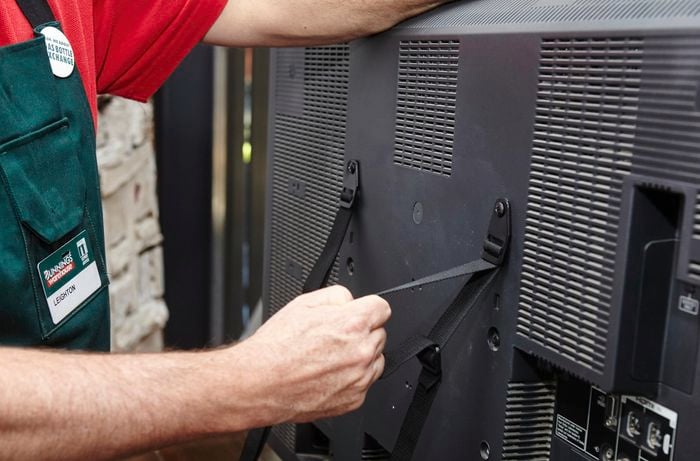 A person attaching safety straps to the back of a television