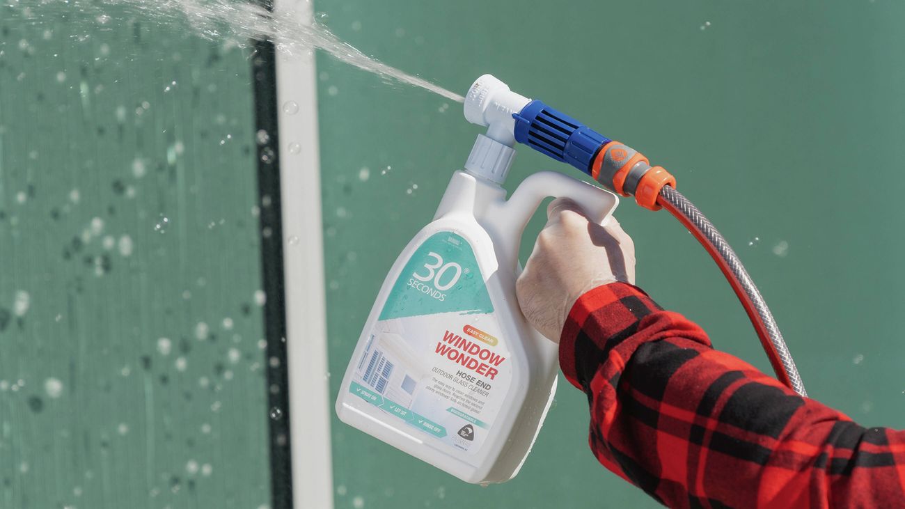A hand holding a hose-end 30 Seconds Window Wonder bottle spraying cleaner onto a window