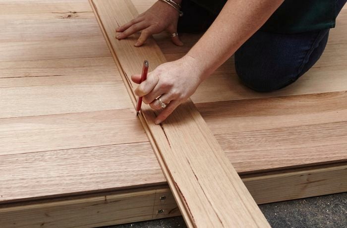 Person using length of timber and pencil to mark up timber bedhead.