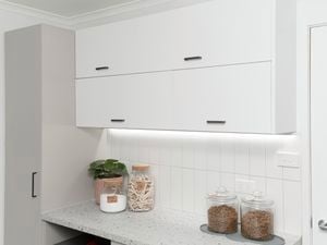 Laundry with lots of cupboards, jars for storage and a plant.