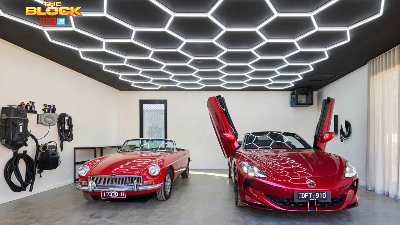 Garage from The Block with hexagonal LED ceiling lights, white walls, and two red sports cars.