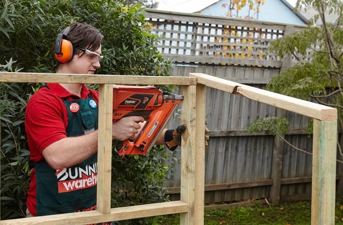 Two sides of a wooden chicken coop frame being nailed together by a Bunnings team member with a nail gun