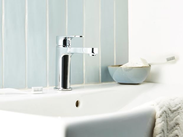 White sink with a bar of soap, a toothbrush and a hand towel on it.