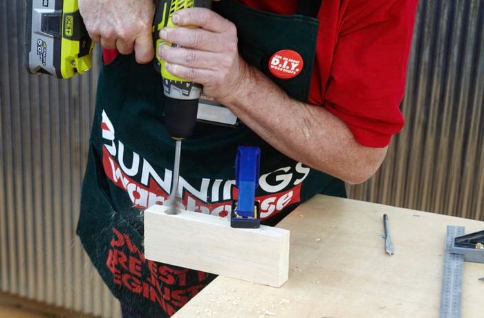 Person drilling hole into piece of timber with spade bit.