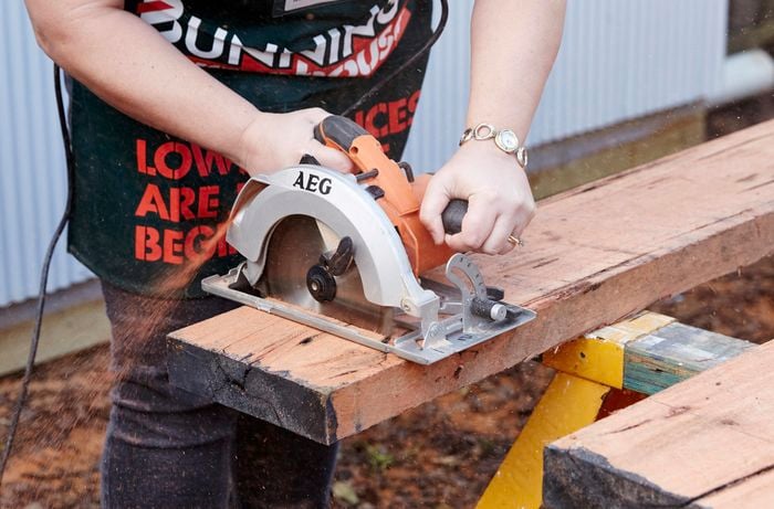 A circular saw cutting through a timber sleeper laying on a painter's horse
