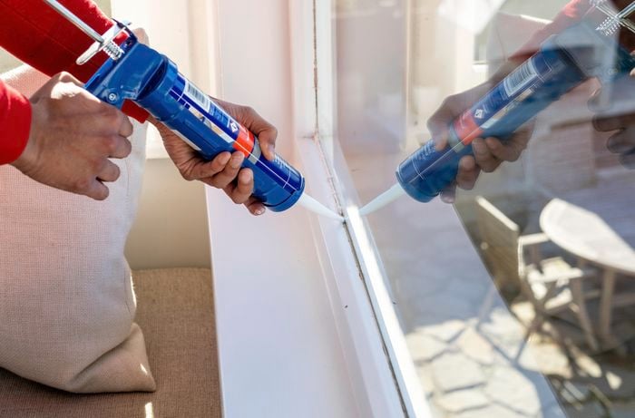 A caulking gun being used to add sealant to a window frame.