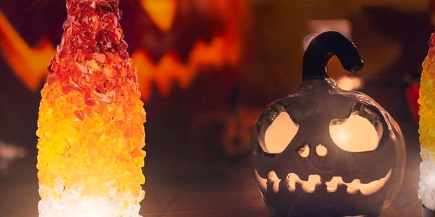 Mosaic lantern in orange, red and clear glass sitting next to a ceramic carved pumpkin candle holder. 
