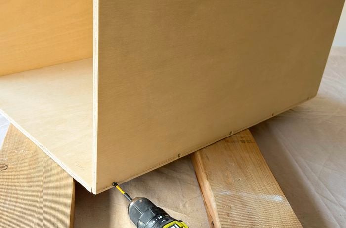 Hands using a drill to assemble a wooden box.
