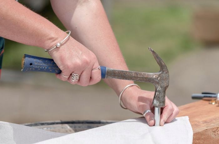 Person making a hole in a sheet of canvas using a hammer and punch