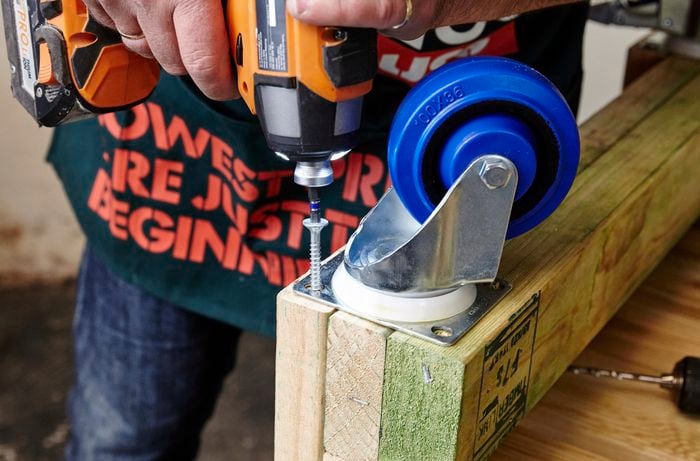 A person attaching a castor wheel to pine framing timber using a cordless drill