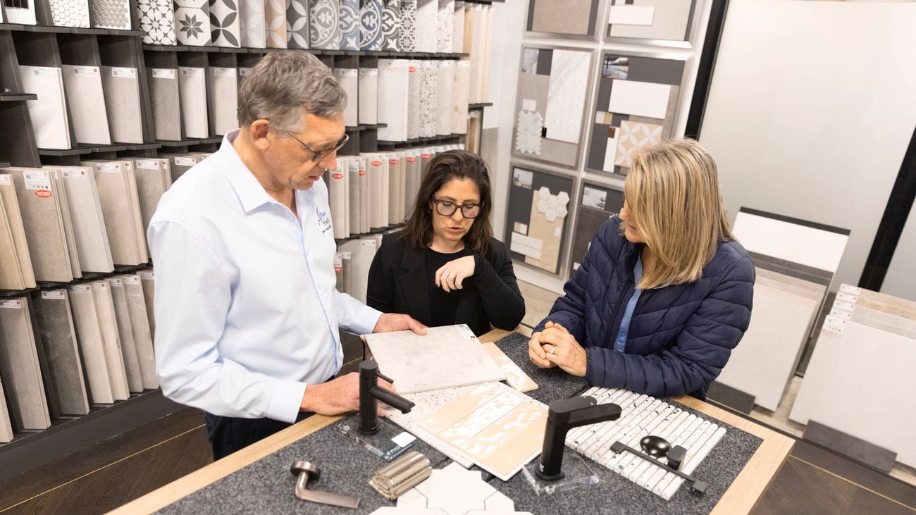 A close-up image of a man and two women - one with dark hair, the other with light hair - looking at tiling and tapware samples on a bench with tiling samples on a wall in the background