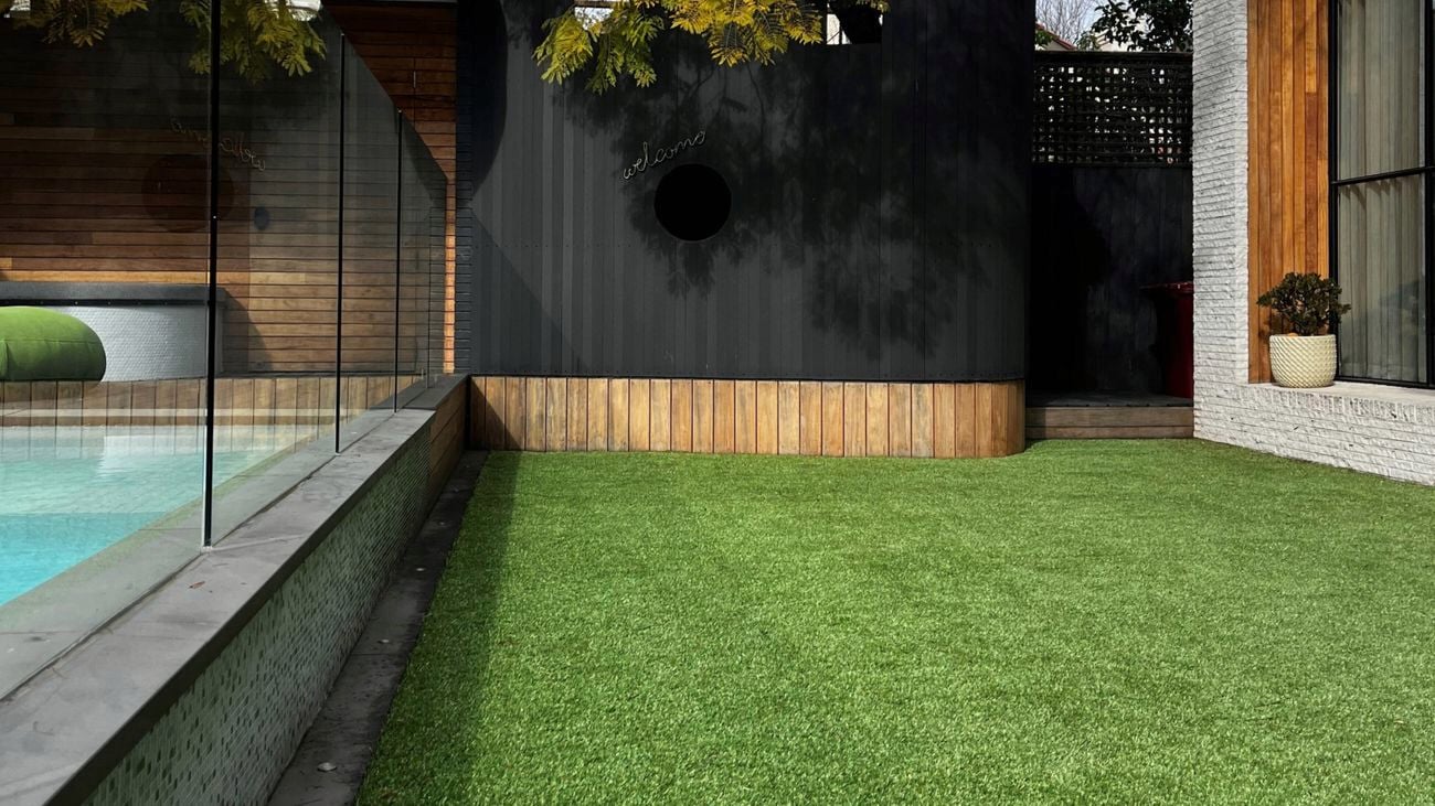 A landscaped backyard featuring a Tuff Turf artificial grass lawn beside a contemporary swimming pool