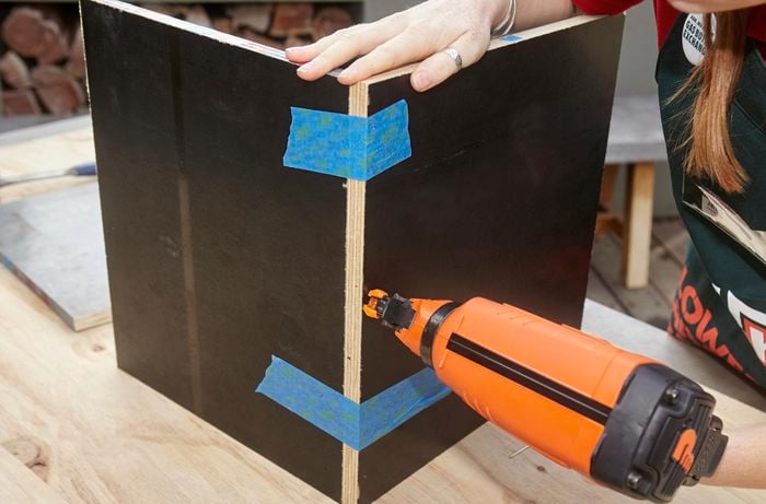 Two side panels of a wooden storage box being nailed together with a nail gun