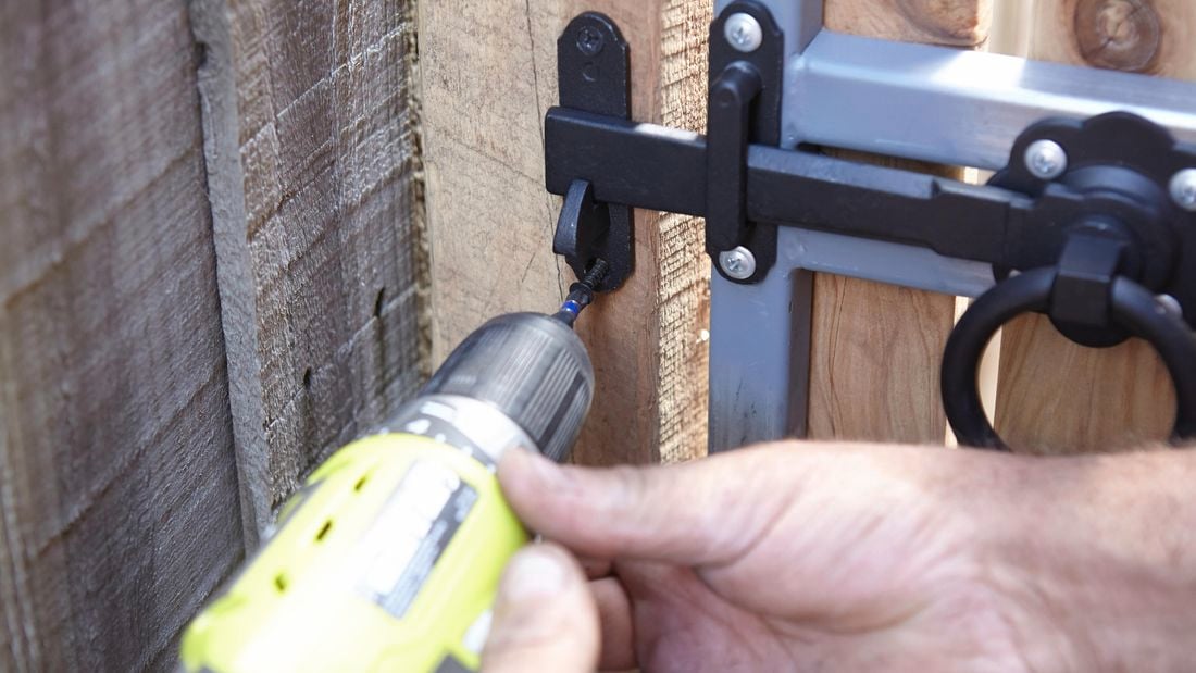 Person screwing a catch plate to a gate post using a cordless driver