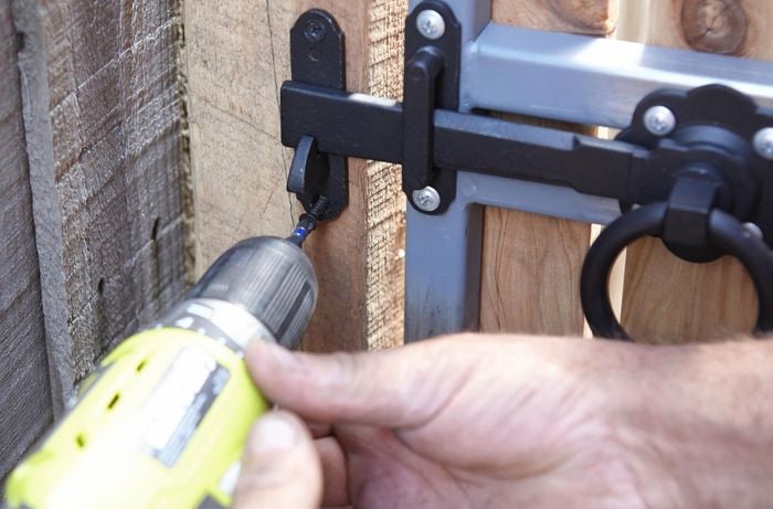Person screwing a catch plate to a gate post using a cordless driver