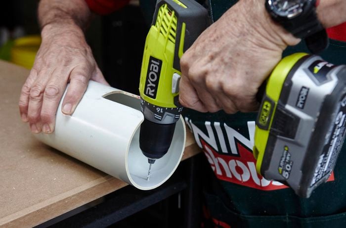A person drilling a hole in a length of PVC pipe using a cordless drill