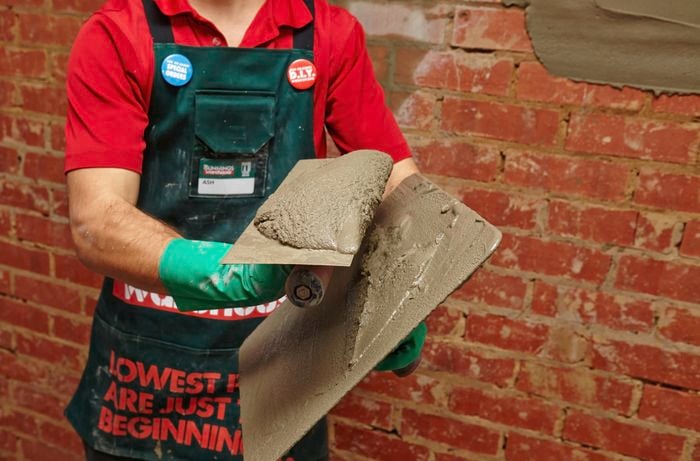 A person scraping plaster from a hawk onto a trowel