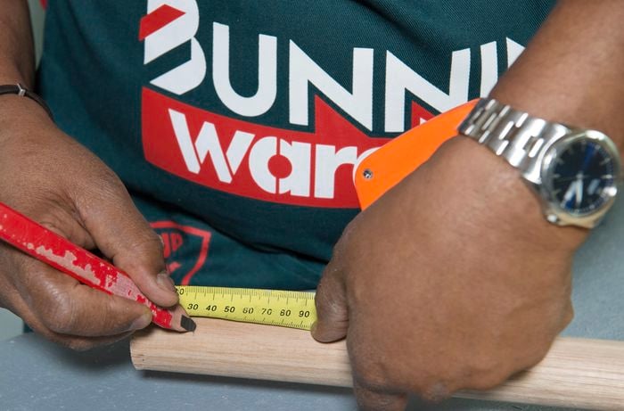 A person marking a length of timber using a measuring tape and pencil