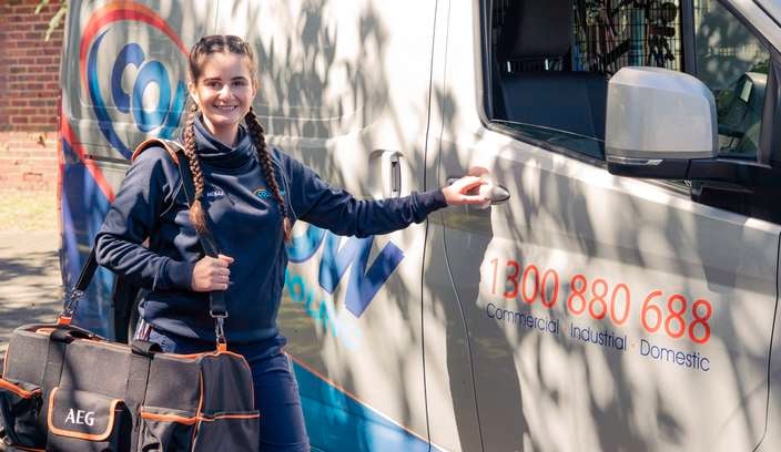A lady holding an AEG black and orange bag, standing next to a van outside.