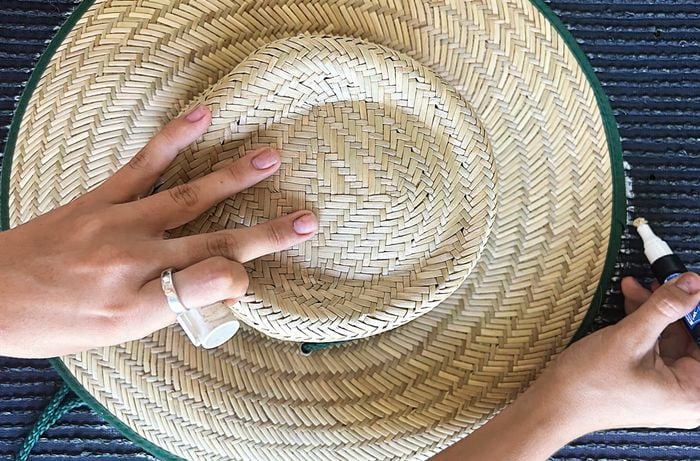 A hand traces around a Bunnings straw hat onto the back of an artificial turf tile with a white marker.
