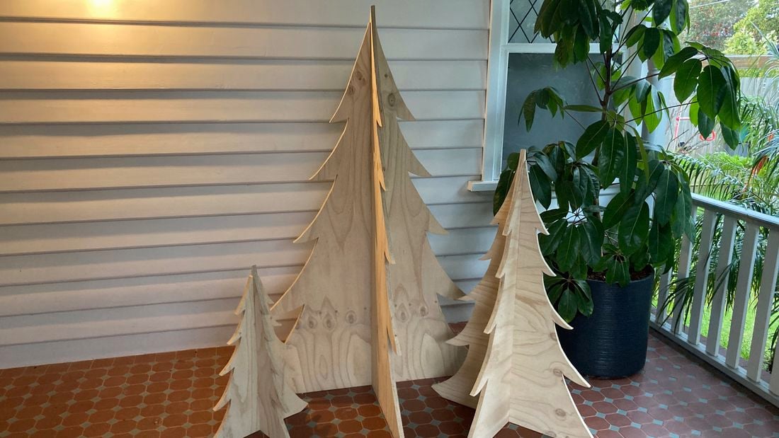 Three plywood Christmas trees of varying sizes placed on a tiled porch next to a potted plant.