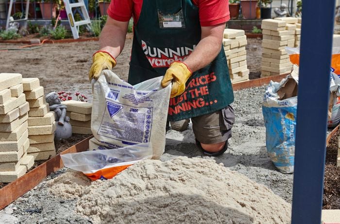 A person emptying a bag of paving sand on to a foundation of crushed rock