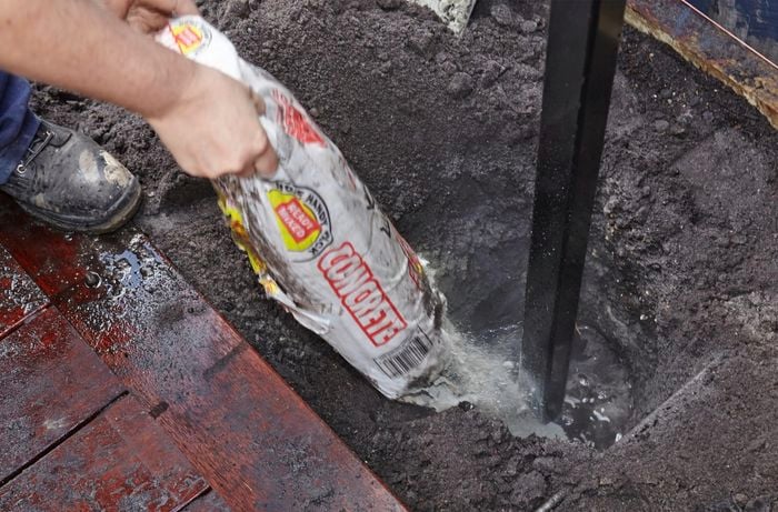 A person pouring ready mixed concrete into a post hole with water in it