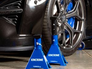Two blue Kincrome 1350kg jack stands near a car's front wheel on a concrete floor.