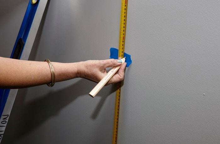 A person with a measuring tape pencilling a mark onto masking tape on a wall