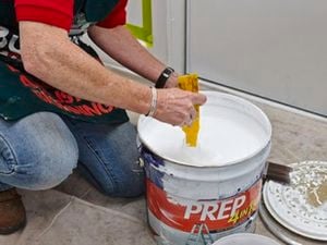 Man in a Bunnings apron stirs a pot of white paint.
