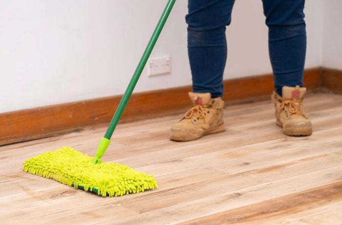 A person is gently mopping the sanded timber floor to clear away dust and debris before applying stain, oil, or protective coating.