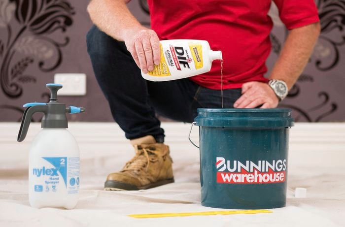 Pouring wallpaper stripper into a bucket.