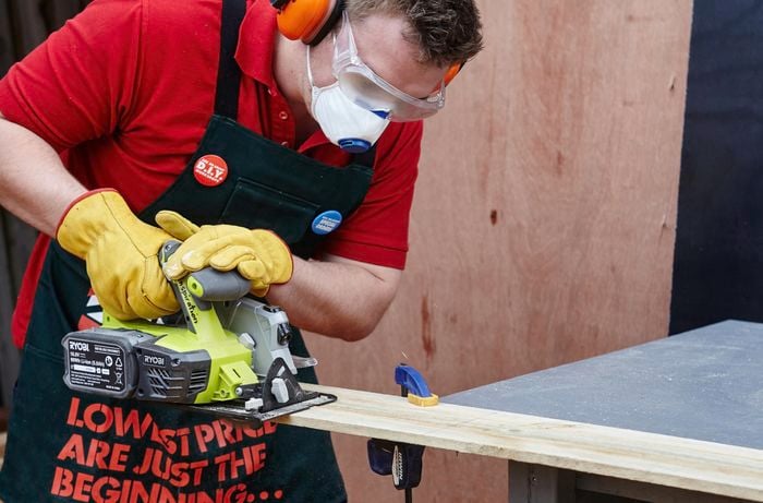 Person using circular saw to cut piece of timber that's clamped to the workbench.