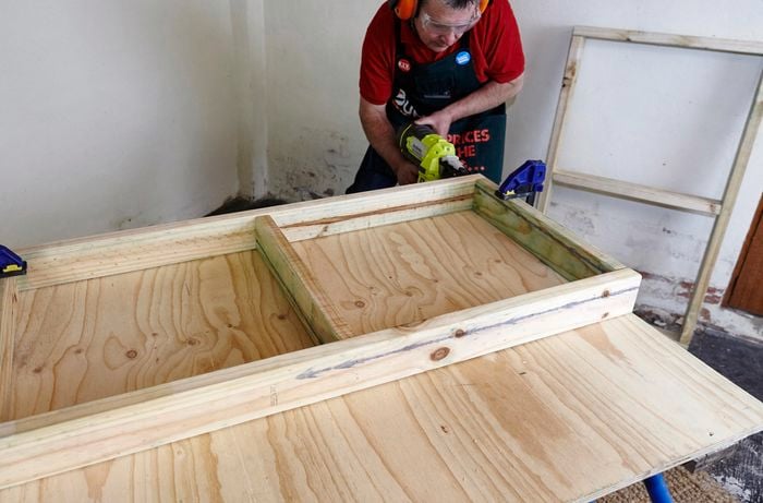 A person using a nail gun to assemble a timber frame