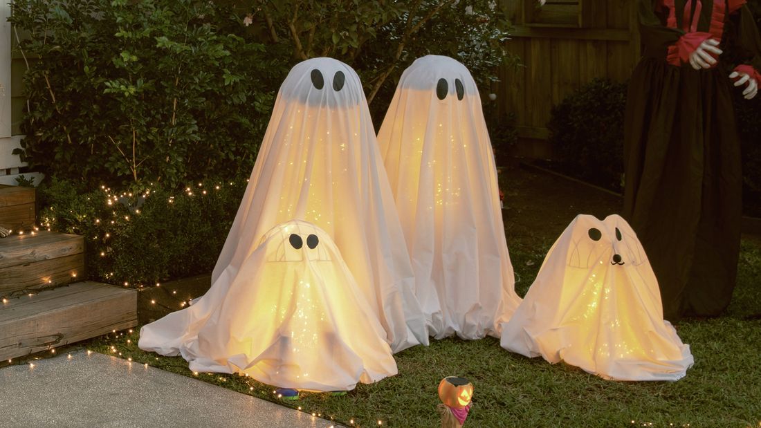 Halloween ghost decorations in a garden at night, surrounded by fairy lights.