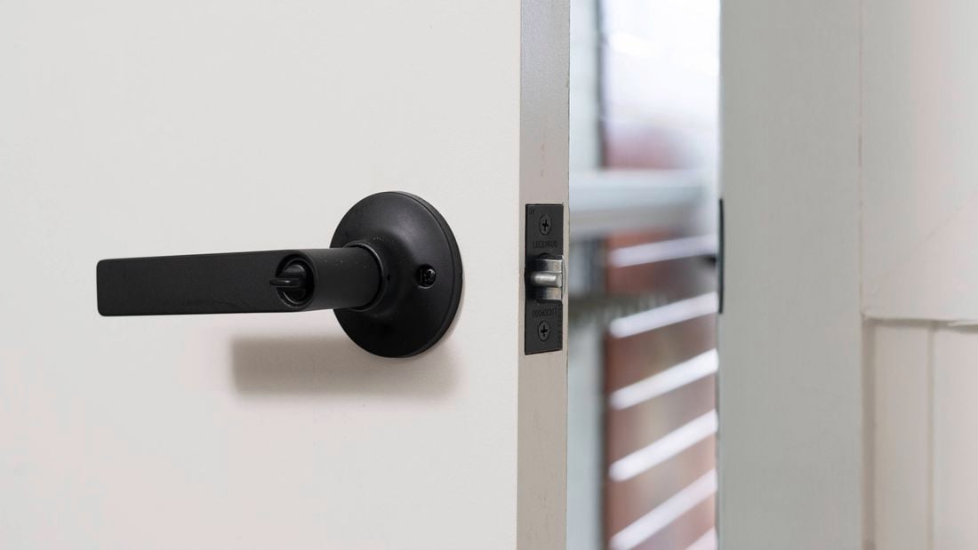 A partially opened white door with a modern black handle and latch.