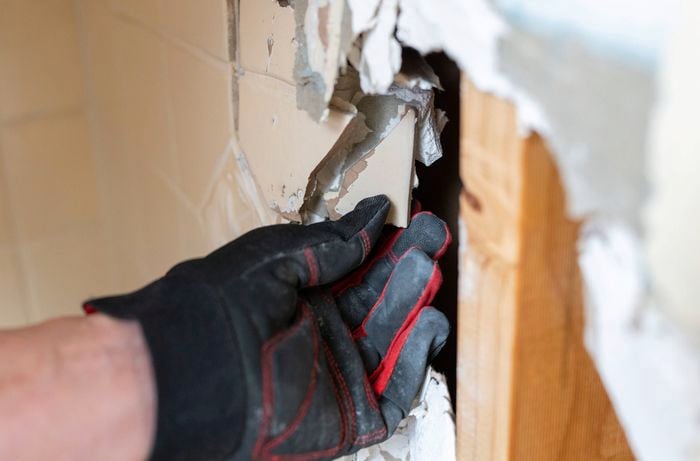 Close up of a hand removing bonded tiles and plasterboard together