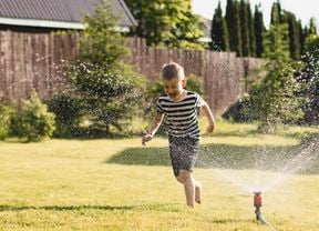 A boy playing under a sprinkler outside.