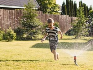 A boy playing under a sprinkler outside.